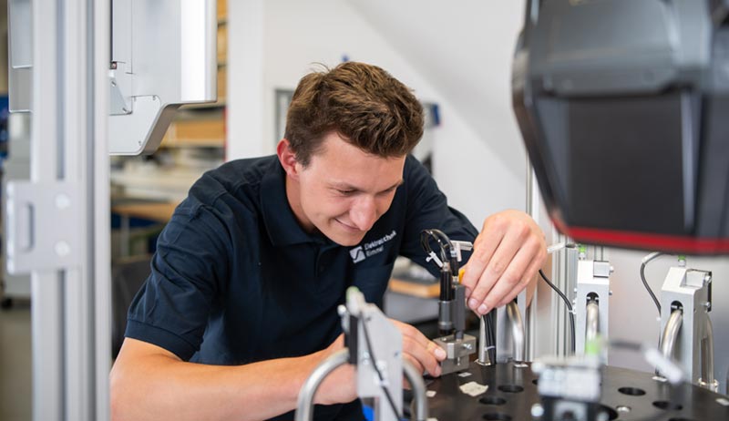 Auszubildender montiert und justiert Baugruppen an einem industriellen Prüf- und Montagesystem